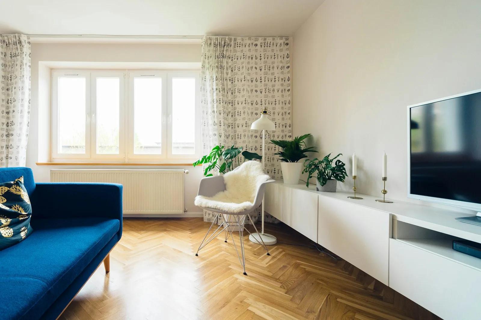A bright furnished living space with a blue sofa, wall-mounted television and herringbone wood floor