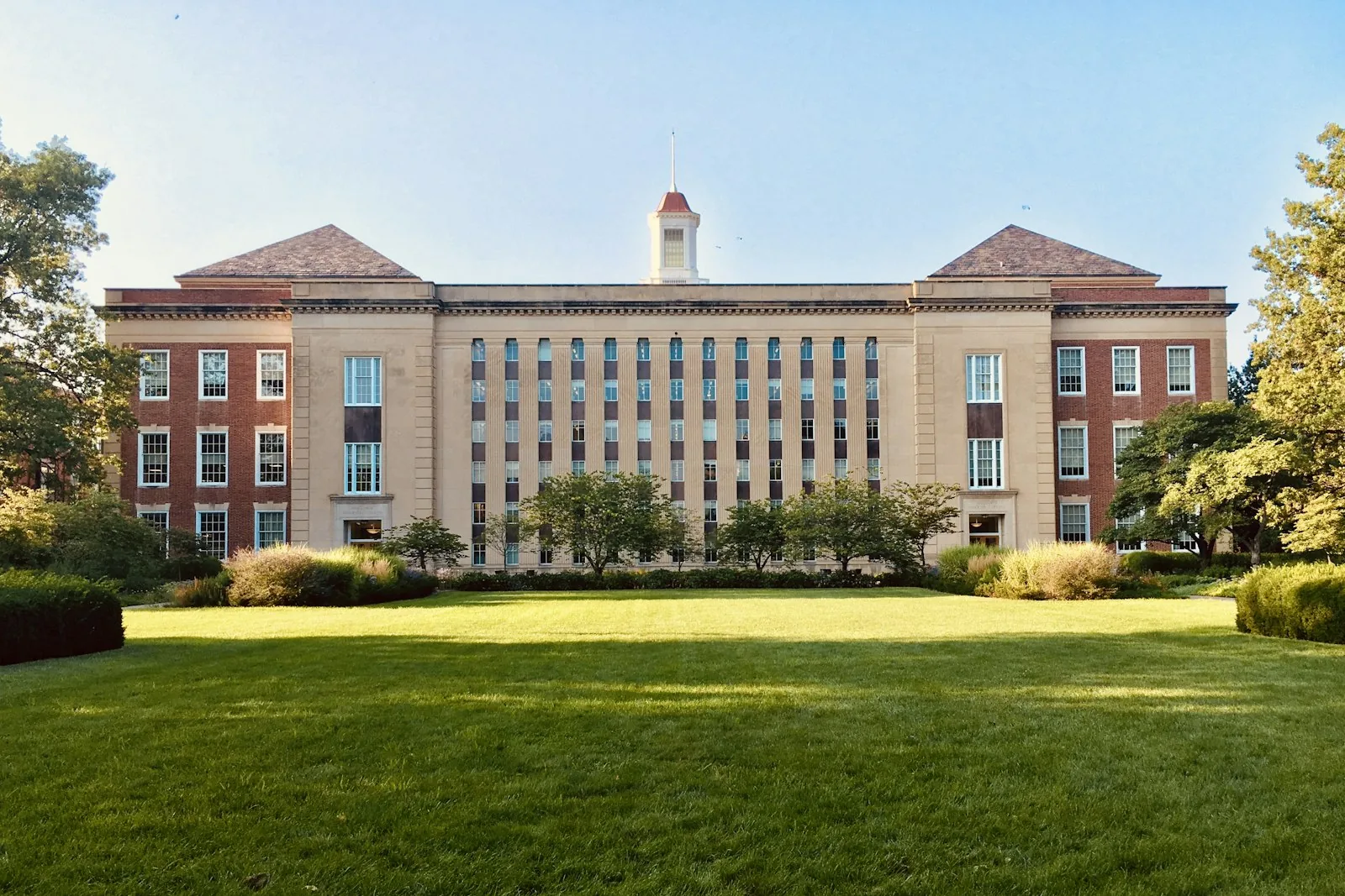 A university building behind a wide green lawn on a clear day